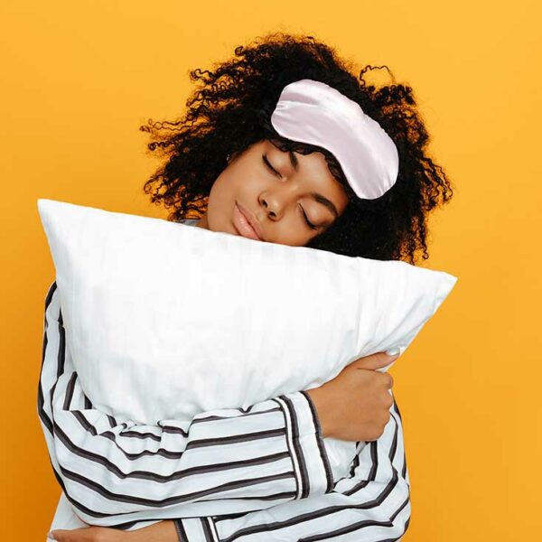 Sleeping. Dreams. Woman portrait. Afro American girl in pajama is hugging a pillow, on a yellow background